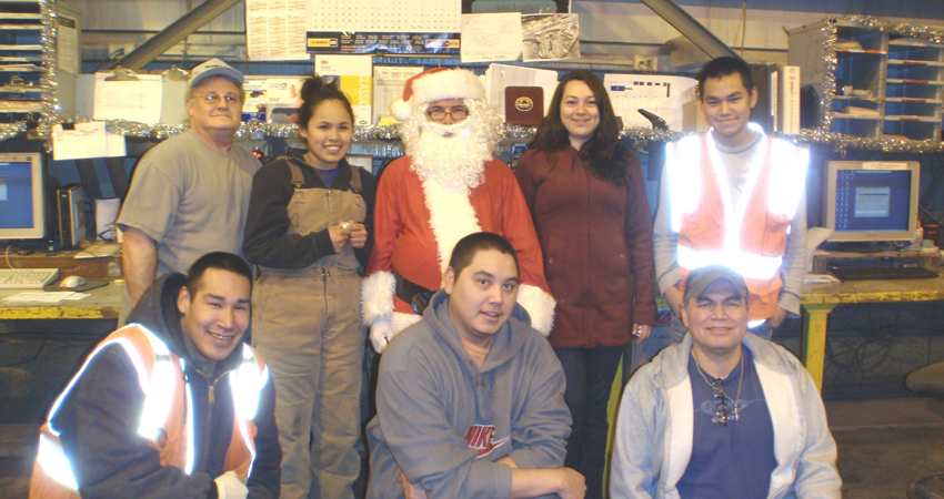 Eight people, one in a Santa costume, posing together in a workplace setting during the holidays.